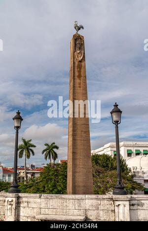 Panama City, Panama - 30 novembre 2008 : obélisque en pierre brune avec statue de coq au sommet du parc français, dans le centre-ville, sous un paysage bleu. Feuillage vert a Banque D'Images