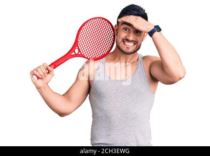 Jeune homme beau tenant une raquette de tennis stressé et frustré avec la main sur la tête, surpris et fâché visage Banque D'Images