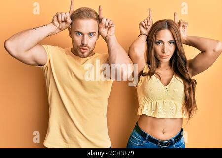 Jeune couple de petite amie et de petit ami qui s'embrasse et se tient ensemble faire un geste drôle avec le doigt sur la tête comme des cornes de taureau Banque D'Images