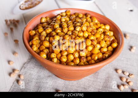 Pois chiches frits aux épices dans une assiette en argile sur fond de bois blanc, gros plan. Banque D'Images