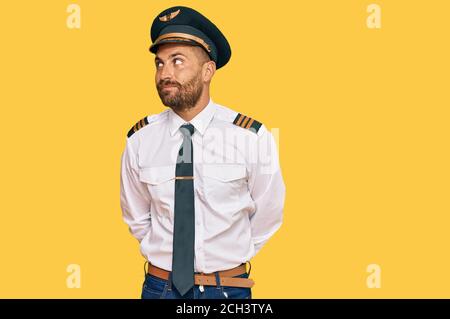 Beau homme avec une barbe portant un uniforme de pilote d'avion souriant regardant sur le côté et regardant loin de penser. Banque D'Images