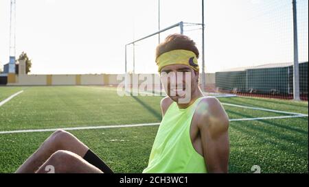 un jeune garçon de vêtements de sport assis sur l'herbe regarde appareil photo Banque D'Images