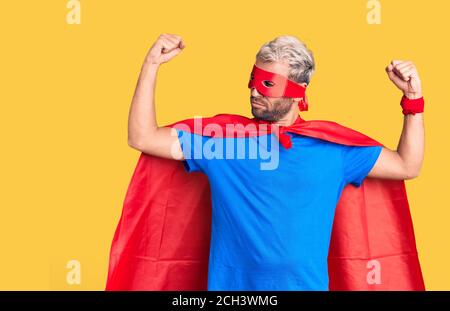 Jeune homme blond portant un super-héros crème montrant les muscles des bras souriant fier. Concept de forme physique. Banque D'Images