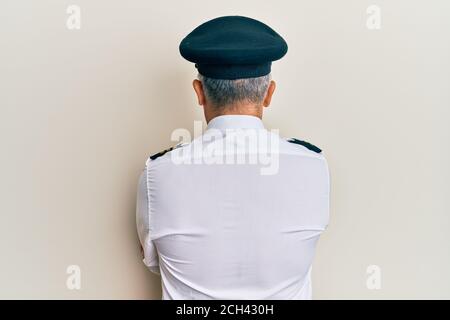 Beau homme d'âge moyen mature portant l'uniforme de pilote d'avion debout en regardant vers l'arrière avec les bras croisés Banque D'Images