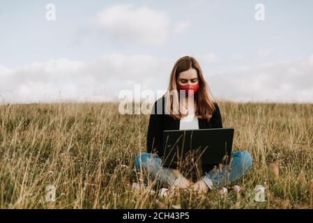 Fille avec masque facial utilisant un ordinateur portable dans un environnement naturel Banque D'Images