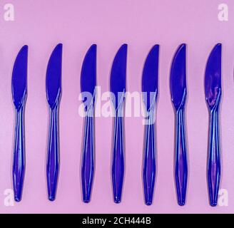 Disposition à plat de couteaux jetables en plastique bleu sur le fond rose Banque D'Images