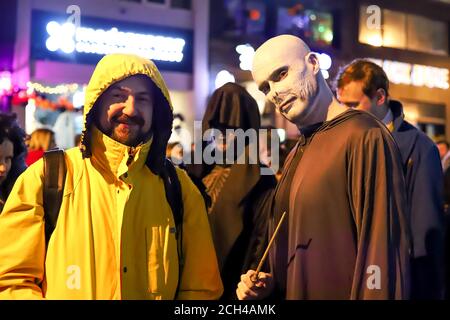 Halloween nuit carnaval . Rue de l'église, personnes marchant dans différents masques et costumes. Banque D'Images