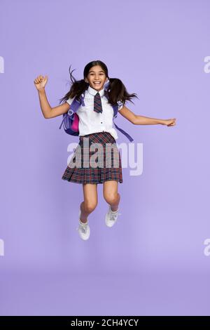 Excitée heureuse école indienne fille sautant isolé sur fond violet. Banque D'Images