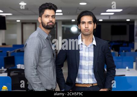 Portrait de deux jeunes hommes d'affaires indiens beaux debout contre le fond du bureau, l'environnement d'entreprise. Banque D'Images