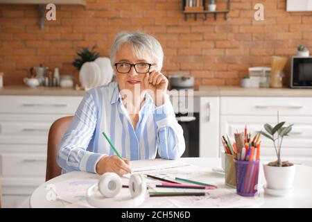 Femme senior coloriant l'image dans la cuisine Banque D'Images