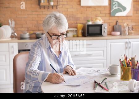 Femme senior coloriant l'image dans la cuisine Banque D'Images