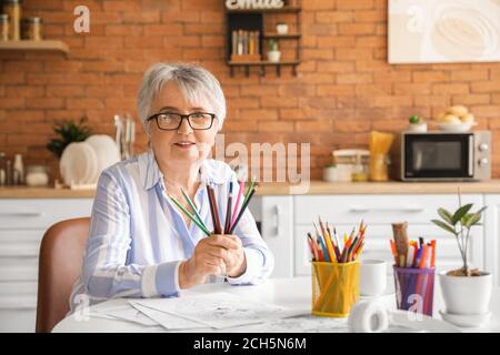 Femme senior coloriant l'image dans la cuisine Banque D'Images