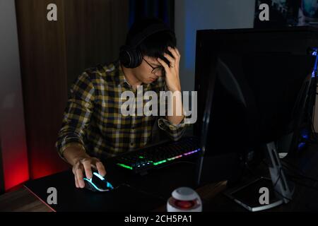 Homme asiatique joueur dans le casque stressé avec la main se sentir déprimé ou en colère choqué en perdant le jeu vidéo sur ordinateur peur et contrarié pour erreur, vi Banque D'Images