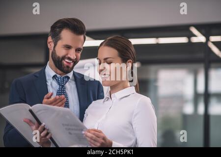 Femme aux cheveux bruns avec un collègue à barbe qui lit des journaux, souriant Banque D'Images