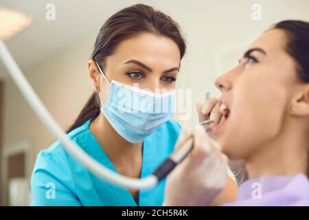 Femme médecin dentiste dans le masque médical faisant le traitement professionnel de dent pour femme en clinique dentaire Banque D'Images