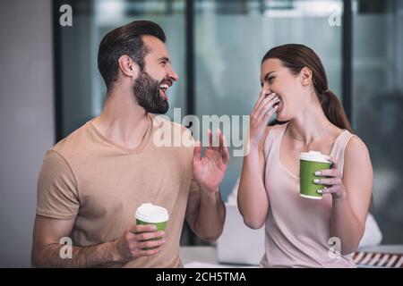 Des collègues masculins et bruns aux cheveux marrons qui apprécient le café, rient Banque D'Images