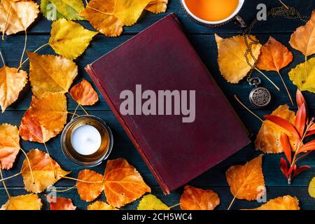 Maquette de couverture de livre d'automne, un vieux livre avec des feuilles d'automne, couché en hauteur sur un fond en bois bleu foncé Banque D'Images