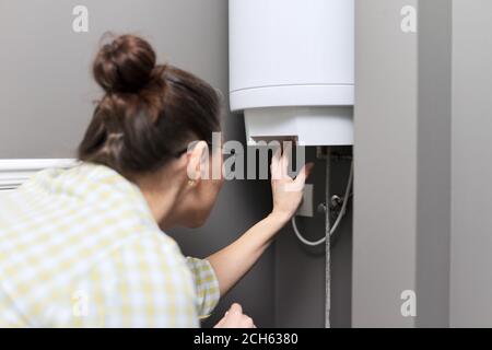 Chauffe-eau domestique, femme règle la température sur un chauffe-eau électrique Banque D'Images