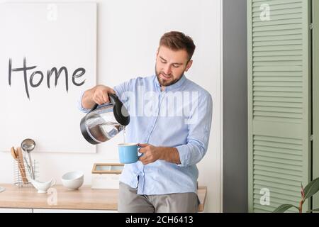 Homme versant de l'eau bouillie chaude de la bouilloire électrique dans la tasse à la maison Banque D'Images