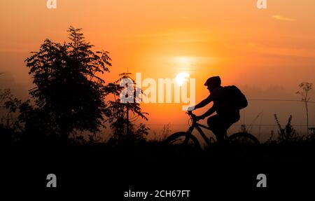 Laatzen, Allemagne. 14 septembre 2020. La silhouette d'un cycliste se distingue contre le soleil levant et contre les champs de brouillard dans le Leinemasch dans la région de Hanovre. Mi-septembre et températures comme en juillet ou août: Une zone de haute pression fournit le temps chaud à la fin de l'été en Allemagne. Credit: Julian Stratenschulte/dpa/Alay Live News Banque D'Images