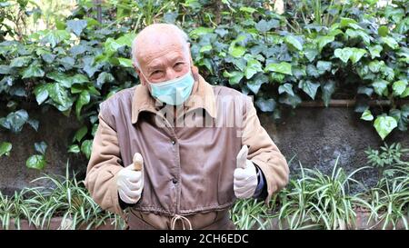 vieux homme dans un masque médical et des gants anti virus covid 19 l'homme âgé montre des gestes de victoire Banque D'Images