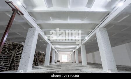 Intérieur de bâtiment industriel avec murs en briques blanches, sol en béton, portes hautes et espace vide pour l'exposition de produits ou l'arrière-plan industriel Banque D'Images