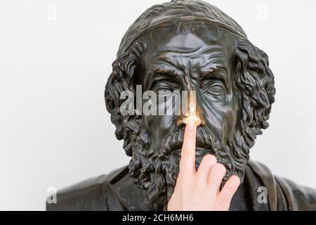 27.10.2018, Saint-Pétersbourg, Russie. Une main femelle pointe vers le nez d'un buste en bronze d'un ancien philosophe. Concept de la connaissance et des musées. Banque D'Images