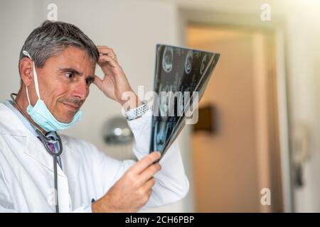 Inquiet médecin de sexe masculin regardant l'acquisition de rayons X à l'hôpital, portant un masque facial. Banque D'Images