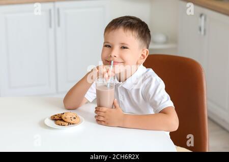 Un petit garçon boit du lait au chocolat et mange des biscuits à la maison Banque D'Images