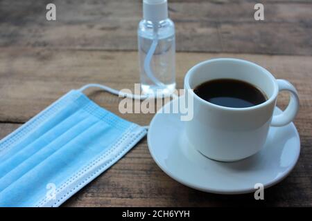 Tasse de café, bouteille de désinfectant pour les mains et masque médical jetable sur table en bois par le dessus. Nouvelle réalité. Copier l'espace Banque D'Images