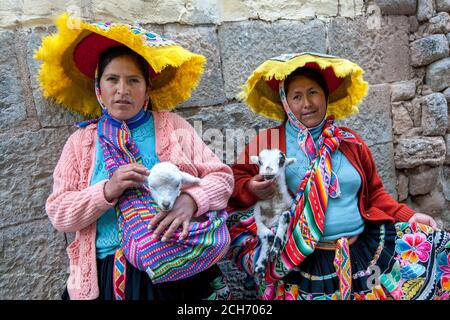 Les femmes péruviennes vêtues de vêtements traditionnels colorés tenant de jeunes agneaux se tiennent contre un mur de pierre dans une rue à Cusco au Pérou. Banque D'Images