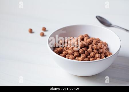 Boules de chocolat flocons de maïs dans un bol blanc, fond blanc. Concept de la nourriture pour le petit déjeuner. Banque D'Images