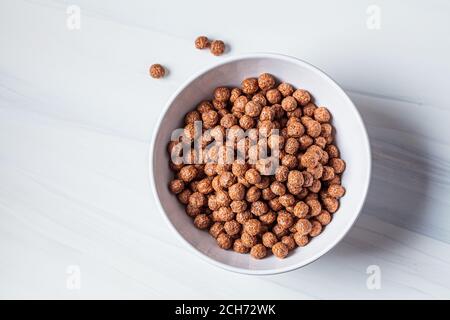 Boules de chocolat flocons de maïs dans un bol blanc, fond blanc. Concept de la nourriture pour le petit déjeuner. Banque D'Images