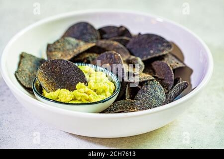 Croustilles noires avec sauce à l'avocat - guacamole, fond blanc. Banque D'Images