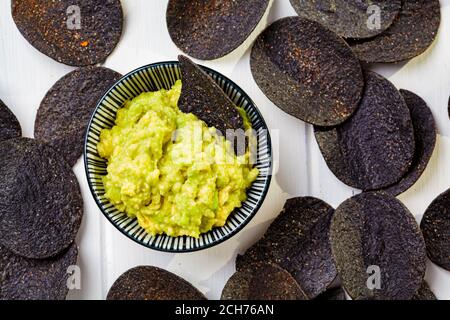 Croustilles noires avec sauce à l'avocat - guacamole, fond blanc. Banque D'Images