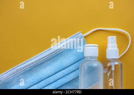 Masque médical jetable et flacons de désinfectant pour les mains sur fond jaune avec espace pour les copies. Trousse de protection contre les pandémies. Banque D'Images