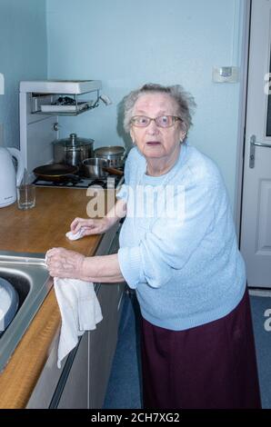 Une femme de quatre-vingt-dix ans vivant seule se lavant dans sa cuisine. ROYAUME-UNI Banque D'Images