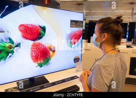 Femme portant un masque de visage regardant la télévision haute définition, écran de télévision dans le magasin. Banque D'Images