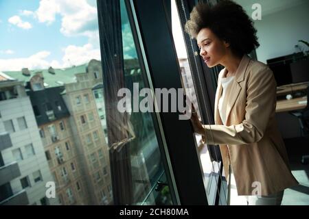 Belle femme d'affaires africaine regardant à l'extérieur de la fenêtre dans le bureau Banque D'Images