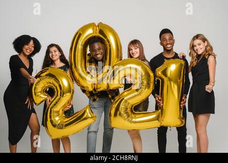 Un groupe de jeunes amis de différentes races célèbrent Noël en studio. Les jeunes gens divers détiennent des numéros d'or 2021 et des sparkers. Banque D'Images