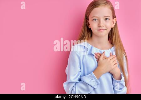 miséricordieux caucasien fille d'enfant exprime des remerciements à la caméra, petite fille avec les cheveux longs posant isolé sur fond rose Banque D'Images