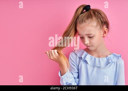 petite fille regarder les extrémités de cheveux fendus isolées, veulent couper les cheveux. fond rose Banque D'Images