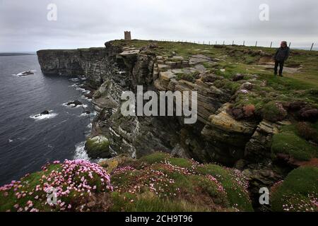 Les visiteurs se promondent le long des falaises au-dessus de la mer à Marwick Head à Orkney, où se dresse la tour construite pour honorer la mémoire de Lord Kitchener. Banque D'Images