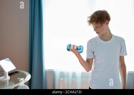 sportive enfant garçon s'exerçant avec des haltères à la maison, jeune garçon caucasien adolescent pompe des muscles de bras Banque D'Images