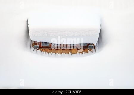 Neige sur le toit d'une maison rurale, glaces suspendues devant la fenêtre. Hiver Banque D'Images