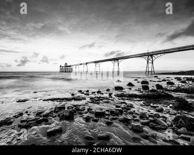 Clevedon Pier, Somerset, au lever du soleil avec galets et rochers en premier plan, avec vue sur les vagues et la mer Banque D'Images