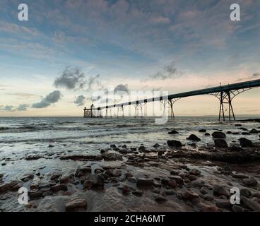 Clevedon Pier, Somerset, au lever du soleil avec galets et rochers en premier plan, avec vue sur les vagues et la mer Banque D'Images