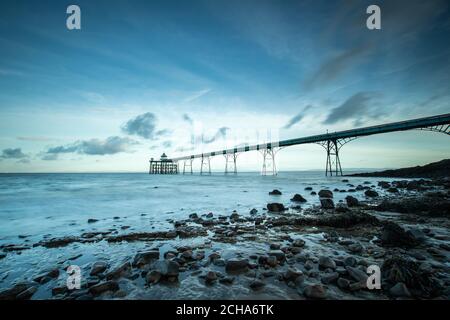 Clevedon Pier, Somerset, au lever du soleil avec galets et rochers en premier plan, avec vue sur les vagues et la mer Banque D'Images