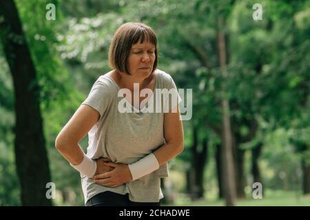 Jogging féminin avec grimace douloureux de visage après avoir ressenti la douleur dans abaisser l'abdomen pendant la course en position de stationnement Banque D'Images