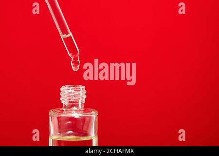 Huile cosmétique, goutte tombe d'une pipette dans une bouteille en verre sur fond rouge Banque D'Images